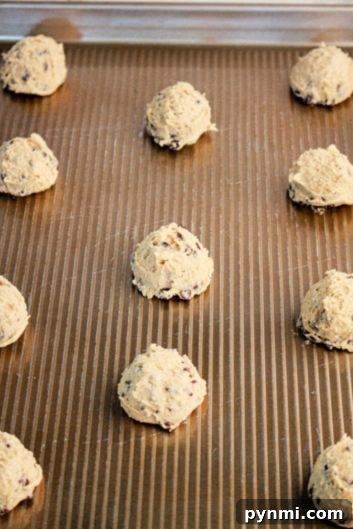 Scoops of cookie dough, crafted from pancake mix, are evenly spaced on a ribbed baking sheet, ready for baking. The dough contains visible chocolate chips.