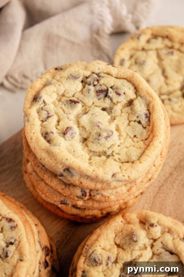 A stack of chocolate chip cookies made with pancake mix sits on a wooden surface. The cookies boast a golden brown color with visible chocolate chips and a slightly cracked texture on top. A beige cloth adds a cozy touch in the background.