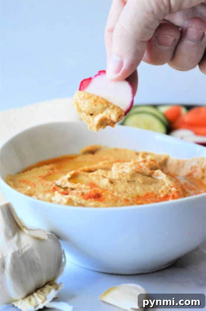 A vibrant bowl of homemade hummus made with canned chickpeas, garnished with fresh herbs and a swirl of olive oil, alongside colorful fresh vegetables for dipping.