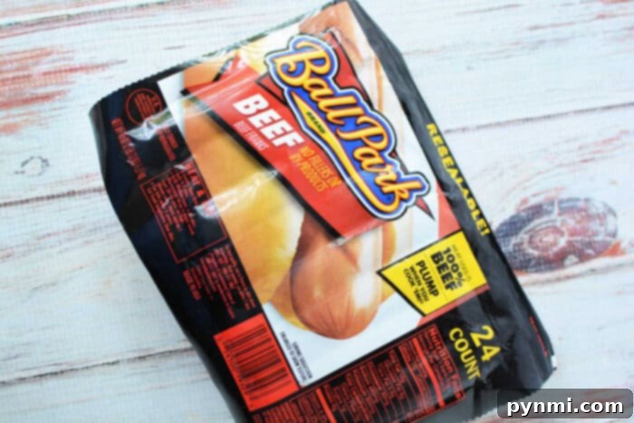 Speedy Slow Cooker Hot Dogs 4 A large, brightly colored package of Ball Park brand beef hot dog buns, featuring "Made with 100% Beef Hot Dogs" prominently displayed. The packaging indicates it contains 24 buns, making it an ideal choice for serving with slow cooker hot dogs at a large party. It rests on a textured wooden surface.