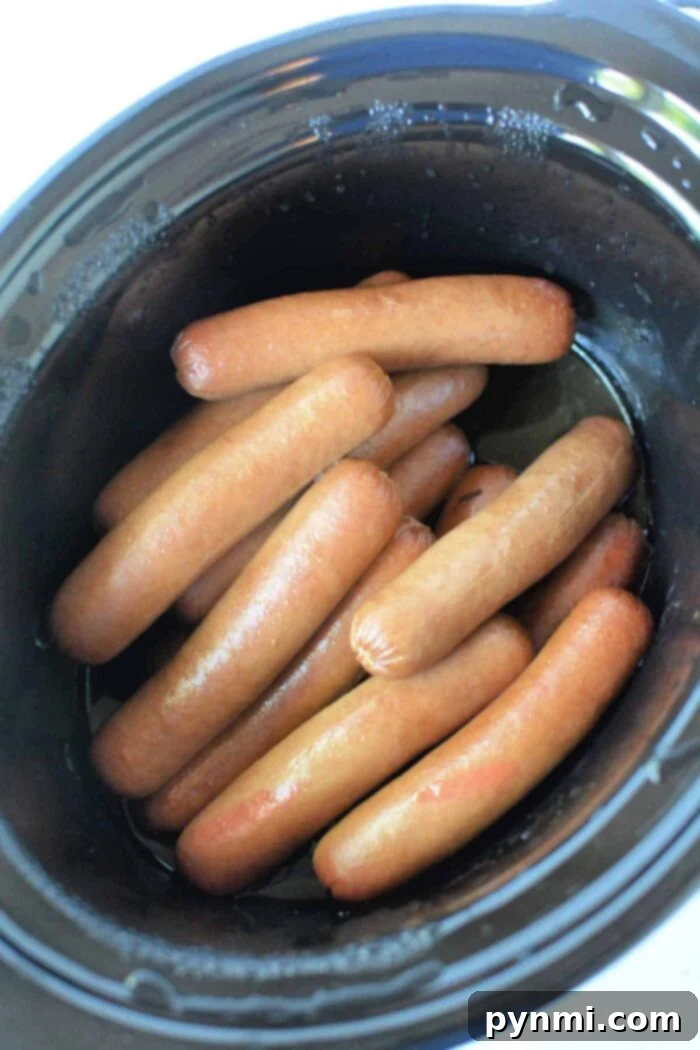 Speedy Slow Cooker Hot Dogs 6 A black slow cooker, brimming with perfectly arranged, slow-cooked hot dogs. The hot dogs exhibit a glossy, light brown hue, indicating they are freshly cooked and ready to be enjoyed.