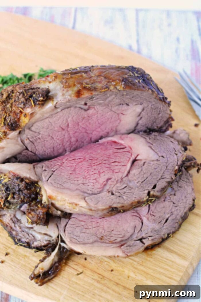 A beautifully sliced boneless rib roast on a wooden cutting board showcases medium-rare perfection in the center with a darker, well-done outer layer. Fresh herbs are sprinkled on top, accompanied by green garnish in the background. A fork is partially visible on the right side, completing this exquisite Boneless Rib Roast Recipe, ready to be served.