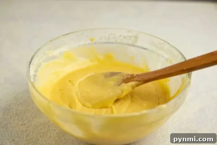 Surprise Pumpkin Loaf Cake 4 A glass bowl filled with yellow cake batter holds a wooden spoon with some batter on it, hinting at the shape inside the soon-to-be baked cake. The background features a light-colored countertop.