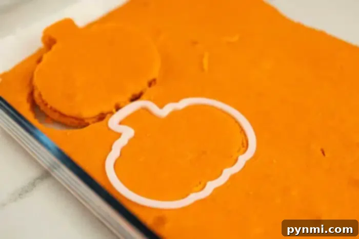 Surprise Pumpkin Loaf Cake 5 A sheet of orange dough with a pumpkin-shaped cookie cutter partially pressed into it. One pumpkin-shaped cut-out is already made and placed beside the cookie cutter. The scene, set on a white countertop, captures the playful process of creating festive shapes inside your kitchen.