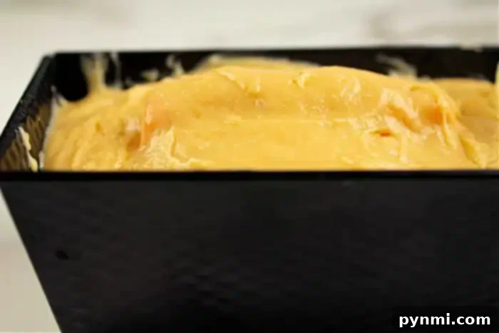 Surprise Pumpkin Loaf Cake 6 A close-up of thick yellow batter poured into a rectangular black baking pan. The batter appears smooth and fills the pan almost to the top, ready for baking, hinting at the delicious shape inside the cake to come.