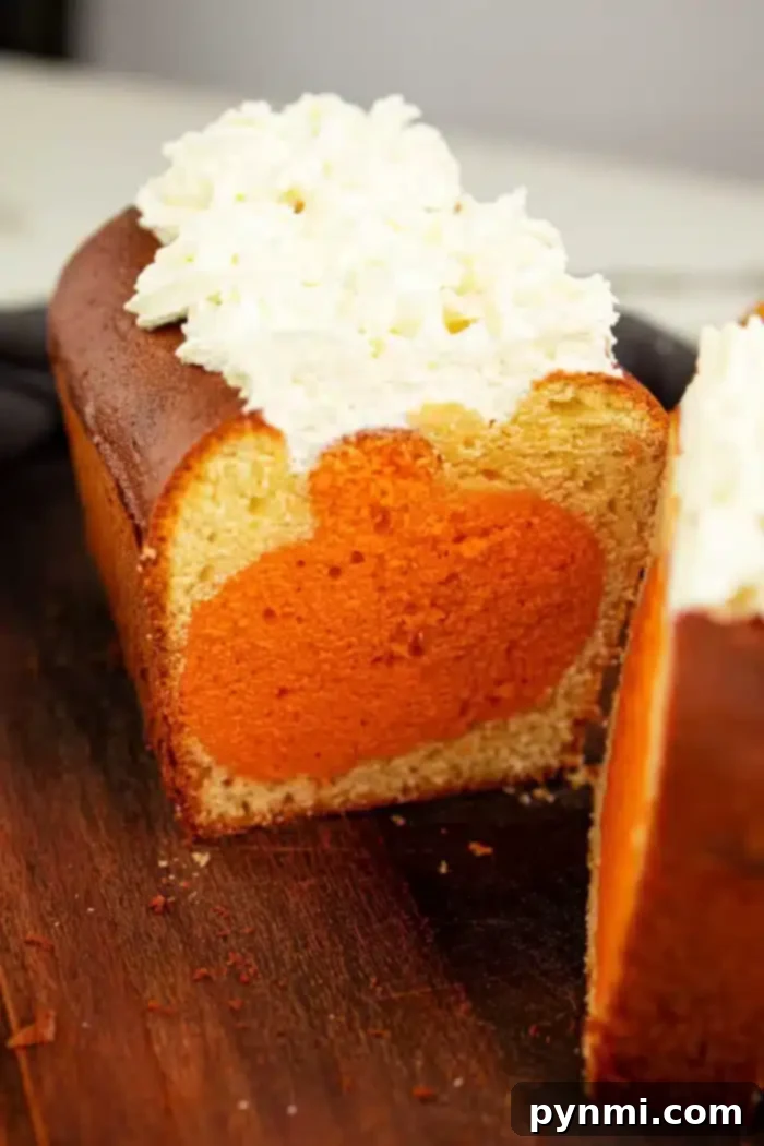 Surprise Pumpkin Loaf Cake 7 A sliced pound cake with a circular orange filling inside the cake. The top of this delightful shape cake is decorated with a generous layer of white frosting. The cake sits on a wooden cutting board.