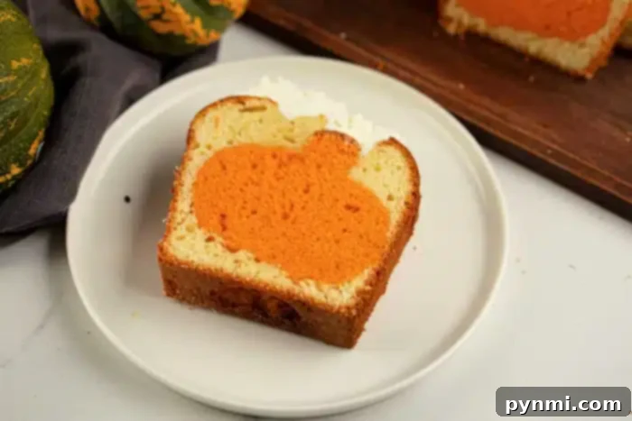 Surprise Pumpkin Loaf Cake 9 A slice of bread loaf on a white plate features an orange pumpkin shape inside the slice. In the background, a wooden cutting board holds another slice of the loaf, accompanied by a cloth and parts of green pumpkins, giving a hint that this might be a charming cake with an intriguing shape inside.