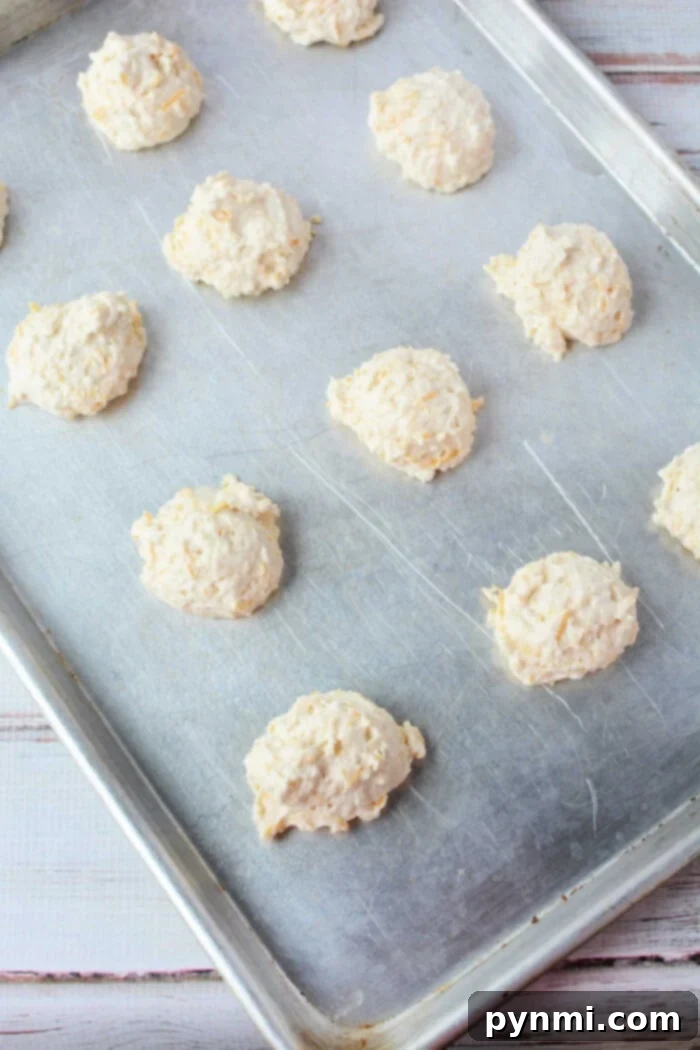 Easy Cheesy Jiffy Biscuits 7 Dollops of Jiffy Mix biscuit dough spaced on a metal baking sheet.