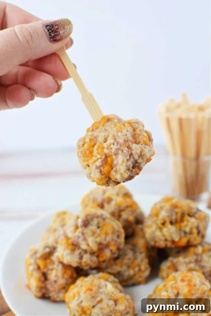 A hand holds a delicate wooden pick, showcasing a perfectly golden-brown cheese and sausage ball, made with Red Lobster Biscuit Mix, poised above a white plate laden with more delectable creations.