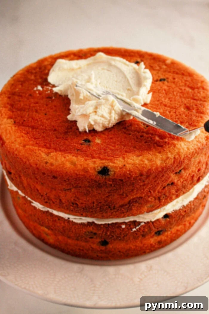 Easy Blueberry Muffin Cake 5 A delightful two-layered cake made with muffin mix and a luscious cream filling, being frosted with a knife on the top layer, elegantly presented on a white cake stand.