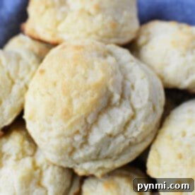 A close-up of freshly baked, golden-brown sour cream biscuits stacked on a blue cloth.