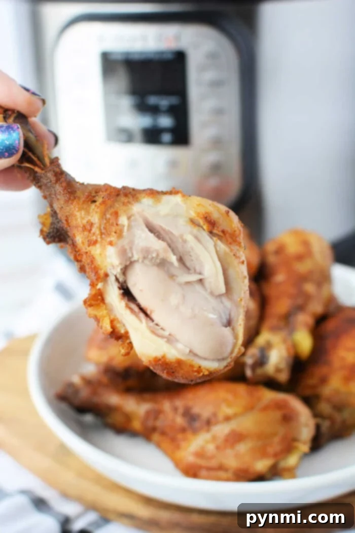 Close-up of a hand holding a juicy piece of pressure cooker fried chicken with visible meat, set against the backdrop of a gleaming pressure cooker.