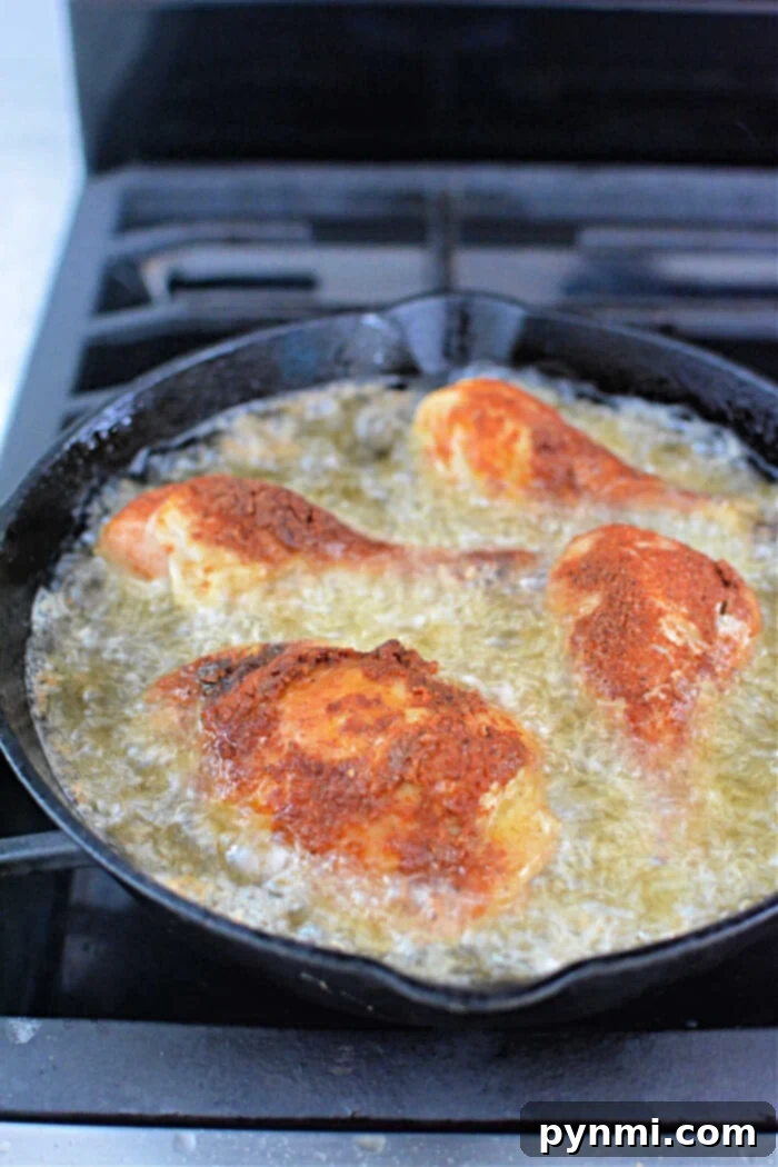 Four pieces of breaded chicken sizzling in a pan, reminiscent of pressure cooker fried chicken, frying to golden perfection with oil on a stovetop.