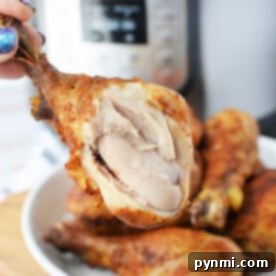 Close-up of a hand holding a juicy piece of pressure cooker fried chicken with visible meat, set against the backdrop of a gleaming pressure cooker.
