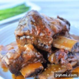 Close-up of a plate featuring mouthwatering braised beef short ribs, simmered to perfection in a pressure cooker and garnished with a rich red sauce, all elegantly presented on a white plate.