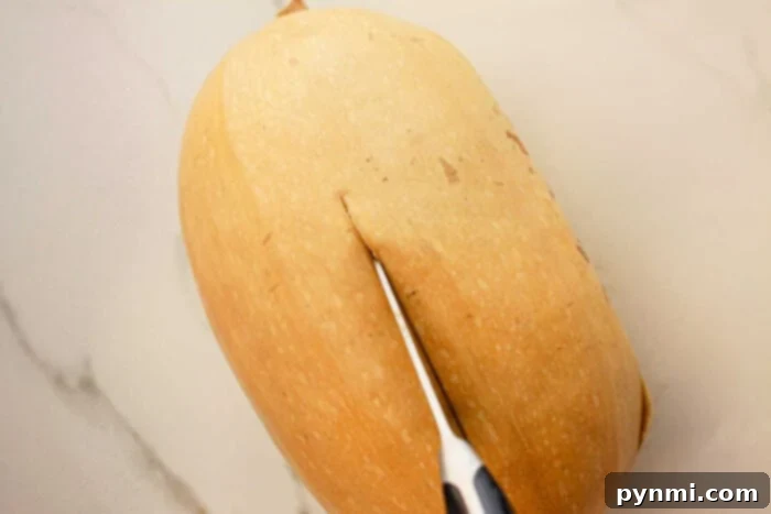 A butternut squash being sliced with a knife on a light-colored countertop, ready to transform into a delicious slow cooker spaghetti squash dish.