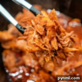 Two-Ingredient Pulled Pork Perfection 6 Tongs holding shredded BBQ pulled pork over a slow cooker, showcasing a delicious, easy 2-ingredient pulled pork recipe.