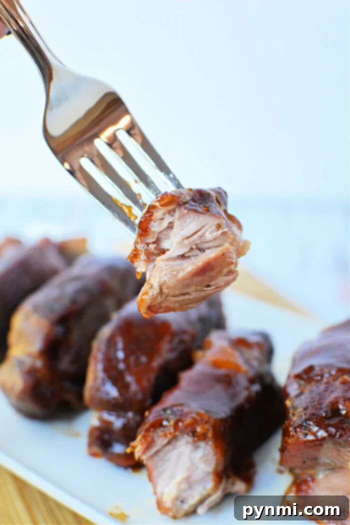 A fork holding a piece of glazed, tender boneless pork ribs above a plate of ribs, showcasing the perfect result of oven cooking.