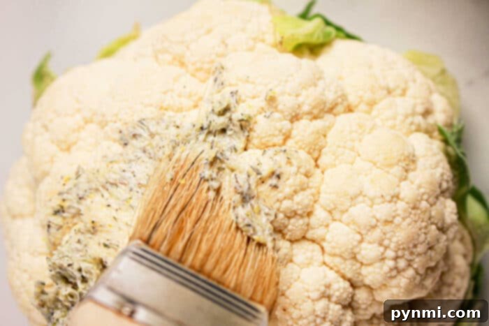 Perfectly Tender Whole Cauliflower Slow Cooker Edition 4 Close-up of a whole cauliflower being brushed with seasoned oil or butter using a flat brush, perfect for a crock pot transformation.