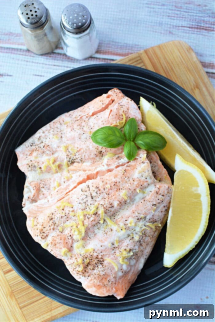 Tender Pressure Cooker Salmon in Minutes 7 Salmon fillets with lemon zest and basil on a black plate, served alongside lemon wedges, salt, and pepper shakers. Perfectly tender, these fillets could easily be mistaken for being made in a pressure cooker.