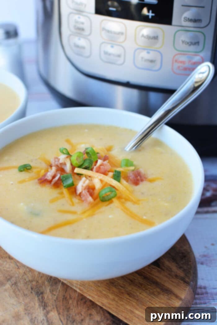 A steaming bowl of creamy Instant Pot potato soup, garnished generously with melted cheddar cheese, crispy bacon bits, and vibrant green onions, with a spoon ready for tasting.