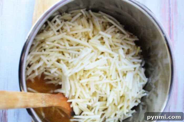A large pot holds a generous amount of shredded potatoes, ready to be transformed into comforting potato soup, with a wooden spoon resting nearby.
