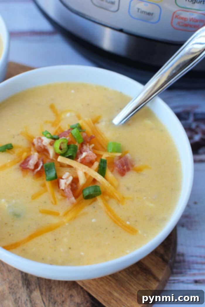 A generously filled bowl of creamy potato soup, topped with crispy bacon bits, rich cheddar cheese, and fresh green onions, sits on a wooden surface. In the soft-focus background, a pressure cooker and a spoon hint at the ease of preparation.