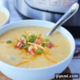 A bowl of creamy potato soup topped with cheese, crispy bacon, and green onions sits invitingly with a spoon beside it, fresh from the pressure cooker.