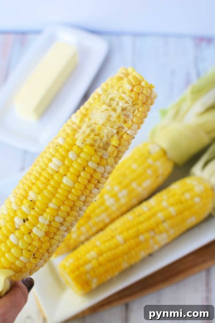 A close-up shows a buttered ear of corn on the cob, with two unbuttered ones and a stick of butter in the background, capturing the essence of oven-cooked perfection.