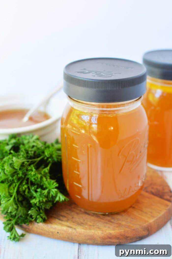Set It and Forget It Slow Cooker Bone Broth 2 Two mason jars of golden bone broth sit on a wooden board, accompanied by fresh parsley, with a white bowl in the background. Perfect for your favorite slow cooker broth recipe.