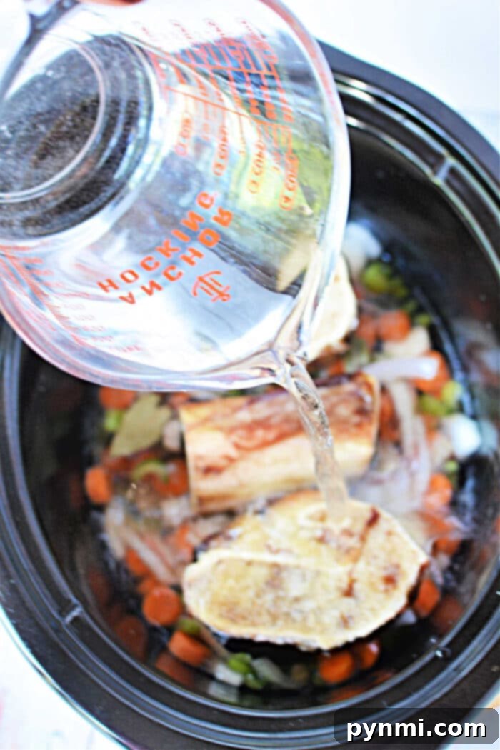 Set It and Forget It Slow Cooker Bone Broth 4 Pouring water into a slow cooker, creating a rich bone broth with vegetables and bones.