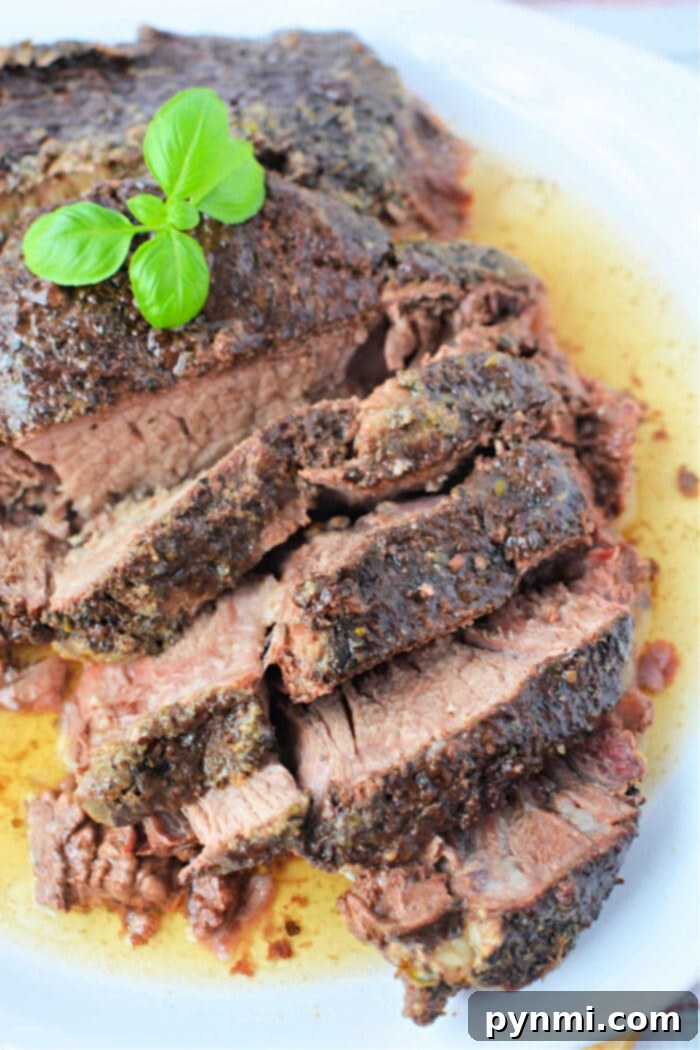 Stovetop Braised Beef 2 Slices of seasoned roast beef, reminiscent of a classic stove top pot roast, are topped with fresh basil on a white plate, surrounded by rich meat juices.
