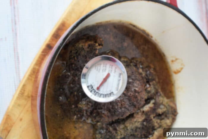 Stovetop Braised Beef 5 A succulent Stove Top Pot Roast sits in a pot on a wooden surface, with a thermometer revealing its perfect temperature of 150 degrees Fahrenheit.
