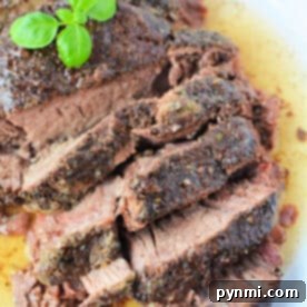 Slices of seasoned roast beef, reminiscent of a classic stove top pot roast, are topped with fresh basil on a white plate, surrounded by rich meat juices.