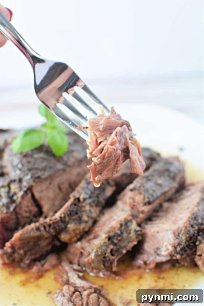 Stovetop Braised Beef 7 A fork holds a piece of sliced, cooked Stove Top Pot Roast above a plate of beef, garnished with a basil leaf.