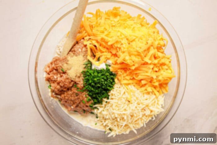Ingredients in a bowl: shredded cheese, herbs, ground meat, and cream mix enticingly, ready to transform into savory sausage balls. A wooden spoon rests on the side, waiting to blend the flavors under the gentle guidance of a pressure cooker.