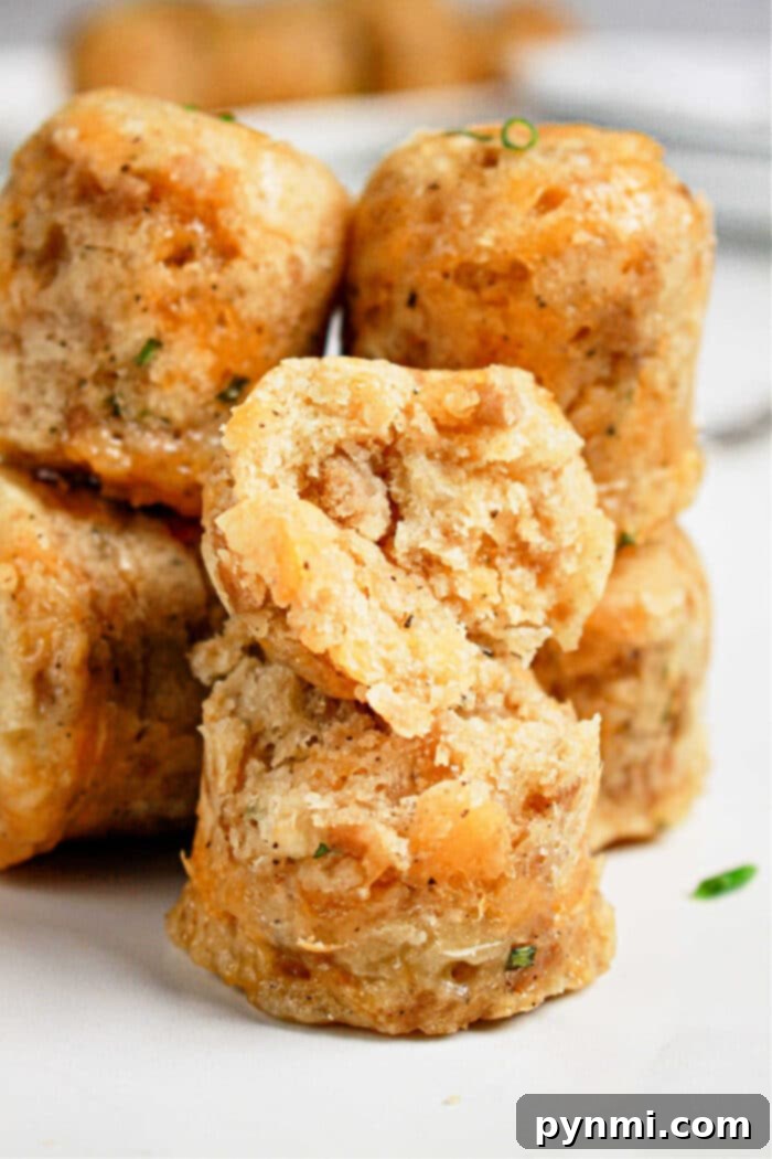 Close-up of stacked, golden-brown savory muffins with a cracked one on top, revealing a soft, textured interior—an inviting sight reminiscent of warm sausage balls fresh from the pressure cooker.