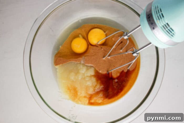 Protein-Packed Perfection Brownies 4 Mixer over a glass bowl with eggs, apple sauce, and batter ready to be mixed for a delicious protein brownie recipe.