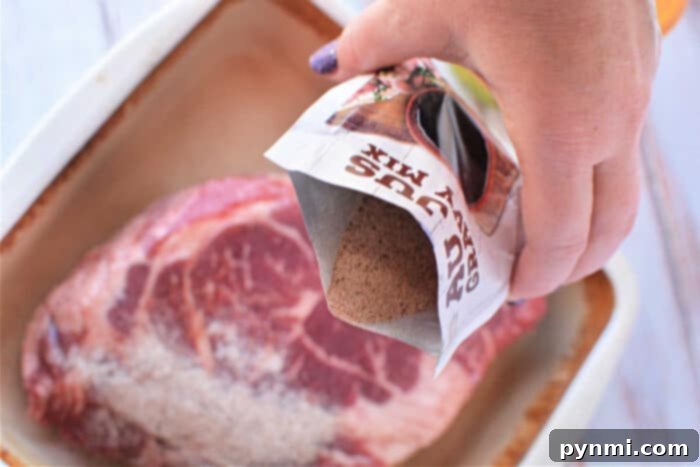 Hand pouring dry gravy mix onto raw steak in a baking dish, this setup hints at the beginnings of a delightful Mississippi Pot Roast recipe.