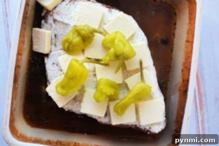 This Mississippi pot roast features a beef roast in a baking dish, topped with butter slices and pepperoncini peppers, creating a flavorful and tender recipe perfect for any occasion.