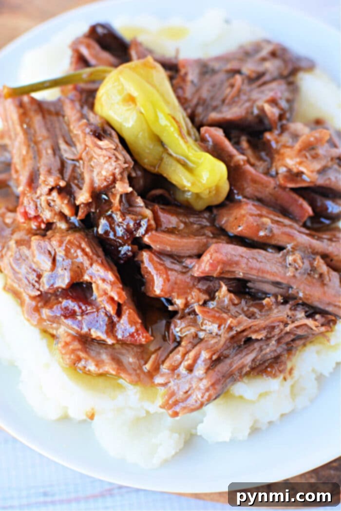 Savor the delightful taste of shredded beef, reminiscent of a classic Mississippi pot roast recipe, atop creamy mashed potatoes with a whole pepper garnish, elegantly presented on a white plate.