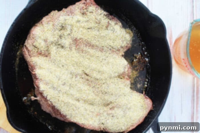 A seasoned boneless beef cut sizzles in a cast-iron skillet, resting enticingly beside a measuring cup filled with aromatic liquid.