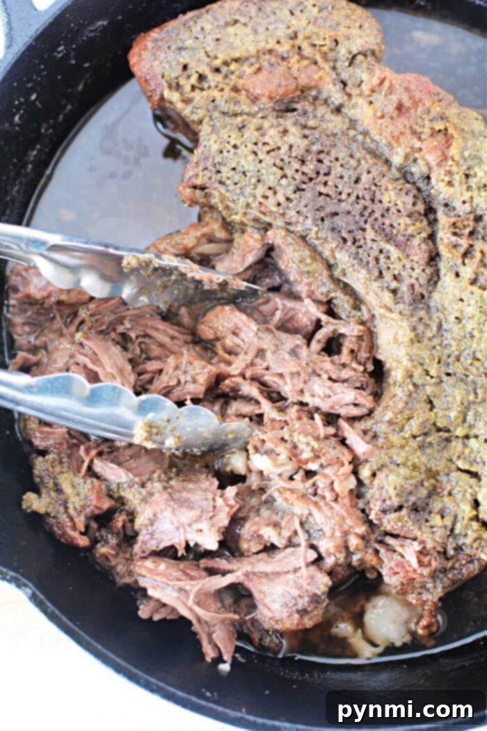 Boneless pot roast shredded with tongs in a cast iron skillet.