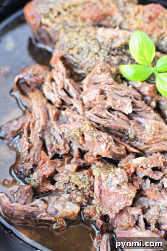 Close-up of shredded boneless chuck roast in sauce, adorned with a garnish of fresh green basil leaves.