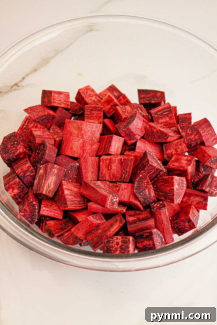 A glass bowl filled with cubed pieces of fresh purple yam, perfect for your next purple sweet potato recipe, rests on a white surface.
