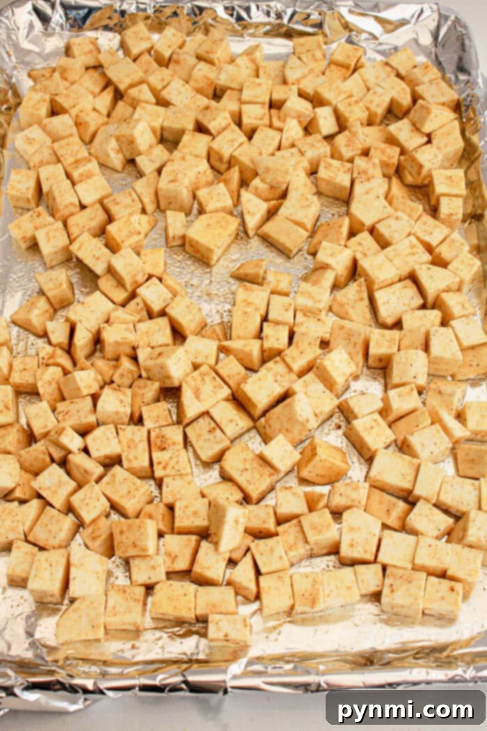White Sweet Potato Delights 5 Cubed sweet potato seasoned and spread on a foil-lined baking sheet, ready to be baked—perfect as a protein-packed addition to any White Sweet Potato Recipe.