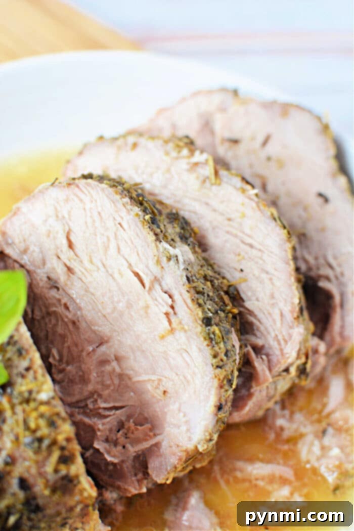 Mouthwatering Slow Cooker Porketta Roast 2 Sliced roasted porketta seasoned with herbs served on a white plate, garnished with a basil leaf.