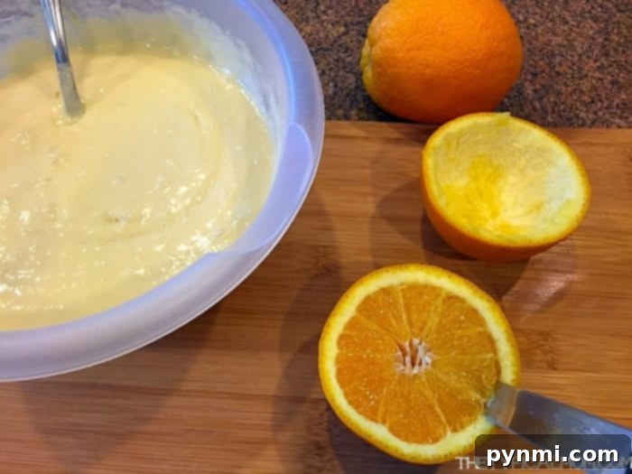 Prepping Ingredients for Grilled Orange Zest Cupcakes A bowl of cake batter with a spoon, alongside a halved orange and a whole orange on a wooden cutting board, illustrating the preparation for grilled orange zest cupcakes.
