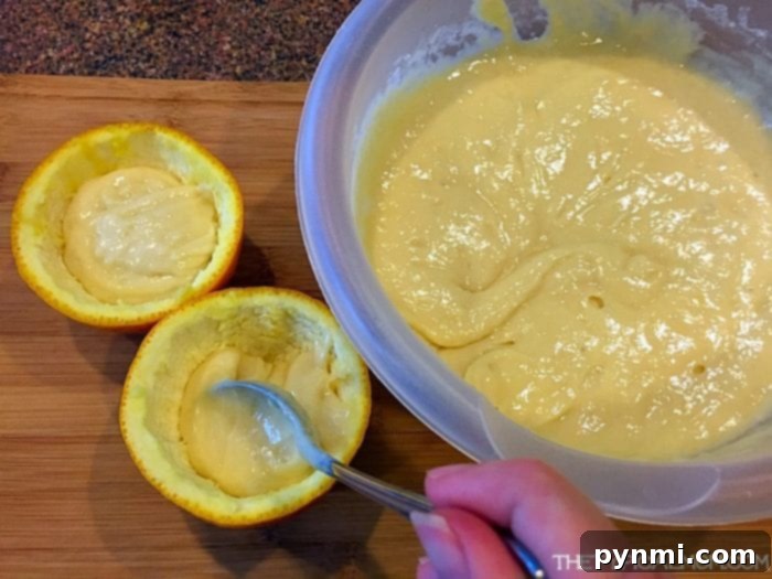 Filling Orange Rinds for BBQ Cupcakes A hand gently fills hollowed orange halves with vanilla cake batter on a rustic wooden cutting board, preparing them for the barbecue.