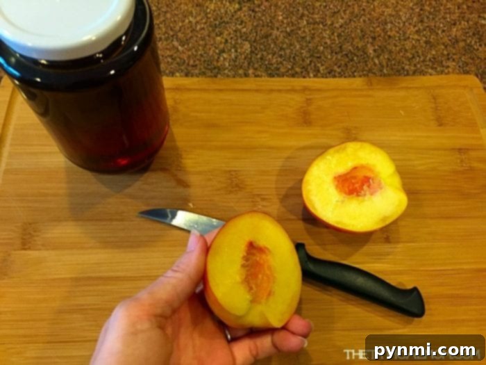 Preparing Fresh Peaches for Grilling A hand holds a perfectly sliced, ripe peach on a wooden cutting board, ready for grilling, with a knife and honey jar in the background.